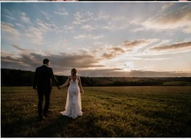 Bride and groom walking through a field at sunset